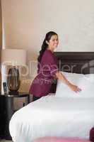 Happy hotel maid fixing pillows