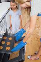 Mother and her daughter taking cookies from the oven