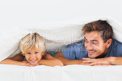 Smiling father and his son lying under the duvet