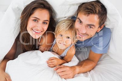 Family smiling under the duvet on the bed