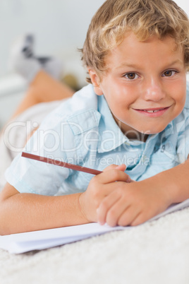 Smiling boy writing lying on the floor