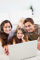 Smiling family lying on a carpet with the laptop