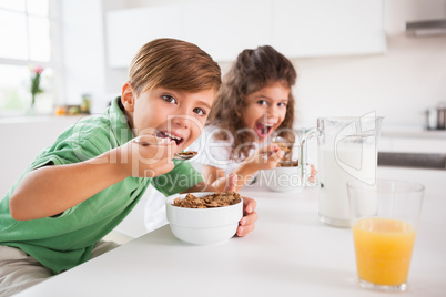 Two children looking at camera while eating cereal