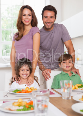 Two children and their parents smiling at the camera at dinner t
