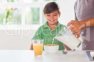 Father putting milk in the cereal of his son