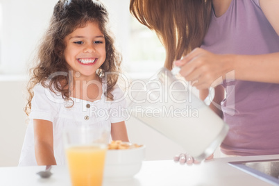 Mother putting milk in the cereal of his daughter