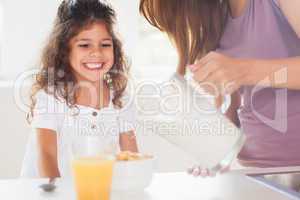 Mother putting milk in the cereal of his daughter