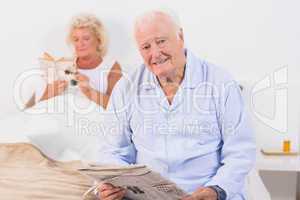 Aged couple looking at camera while reading