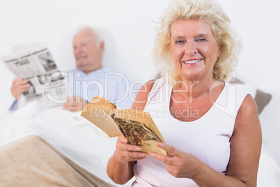 Smiling old couple reading book and newspaper