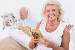 Smiling old couple reading book and newspaper