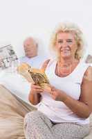 Smiling aged couple reading book and newspaper