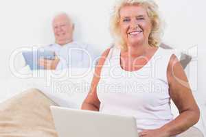 Smiling aged couple using a tablet and the laptop