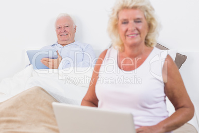 Smiling old couple using a tablet and the laptop