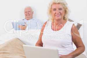 Smiling old couple using a tablet and the laptop