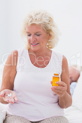 Smiling aged woman with the opened pill bottle