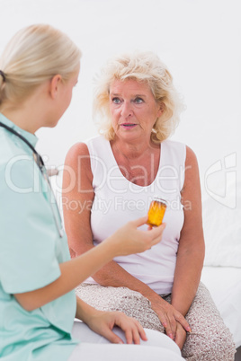 Home nurse showing a pills bottle to her patient