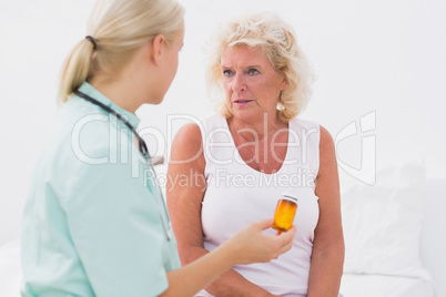 Home nurse showing a pill bottle to her patient