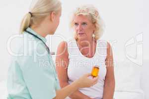 Home nurse showing a pill bottle to her patient