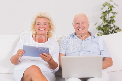 Smiling old couple using a laptop and the tablet