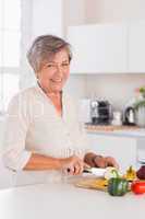 Old woman cutting vegetables on a cutting board with a smile