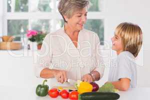 Grandmother cutting vegetables looking at her grandson