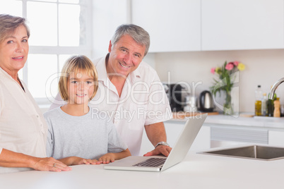 Child and grandparents looking at the camera with a laptop in fr