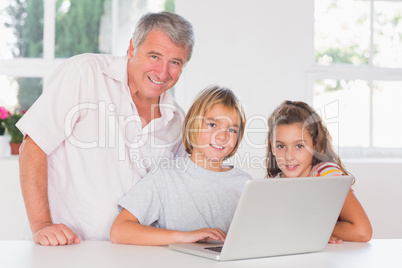 Grandfather and children looking at the camera with laptop in fr