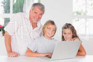 Grandfather and children looking at the camera with laptop in fr