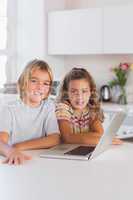Two children looking at the camera with laptop in front