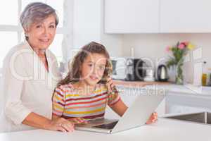 Grandmother and little girl looking at the camera with laptop