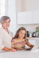 Smiling grandmother and child looking at the camera with laptop