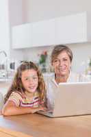 Smiling child and granny looking at the camera with laptop