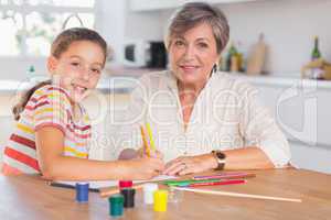 Child with her grandmother looking at the camera while drawing