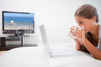 Woman taking a sip of coffee while surfing the internet in the l
