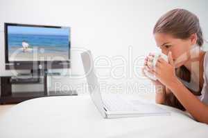 Woman taking a sip of coffee while surfing the internet in the l