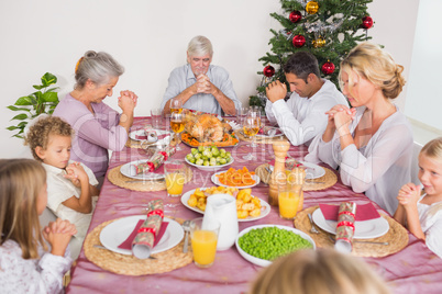Family saying grace before christmas dinner