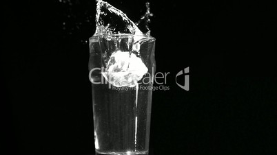 Ice cube dropping into glass of water