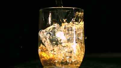 Whiskey being poured into a glass with ice cubes