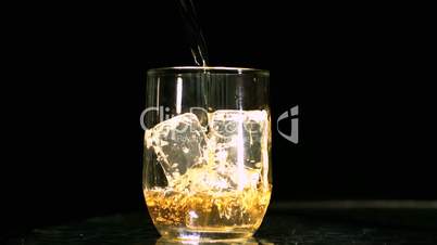 Whiskey being poured into a glass with three ice cubes
