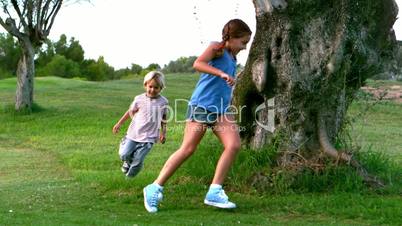 Little girl and little boy running around a tree