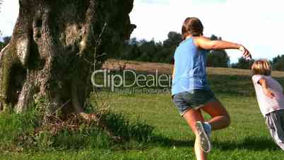 Little girl running after a little boy around a big tree