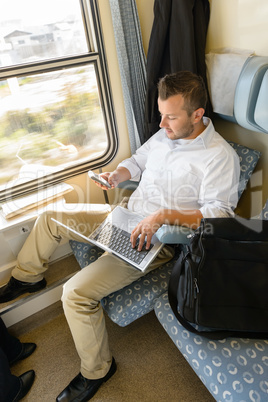 Man texting on phone holding laptop train