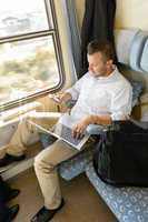 Man texting on phone holding laptop train