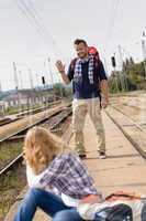 Man waving to woman sitting on railroad