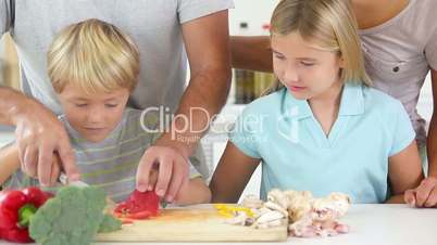 Mother and daughter watching father and son slicing vegetables
