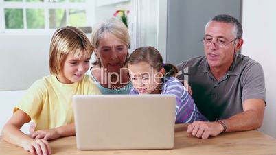 Brother and sister looking at laptop with grandparents
