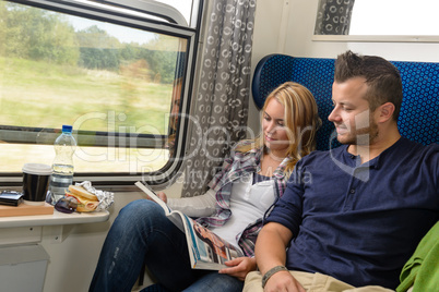 Couple traveling by train reading magazine smiling
