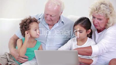 Two grandparents and two children using a laptop