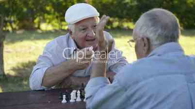 Active retired seniors, two old men playing chess at park