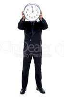 Executive holding up wall clock in front of his face